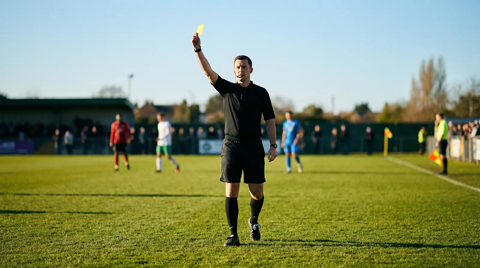 Árbitro de fútbol mostrando una tarjeta amarilla en un campo de césped durante un partido