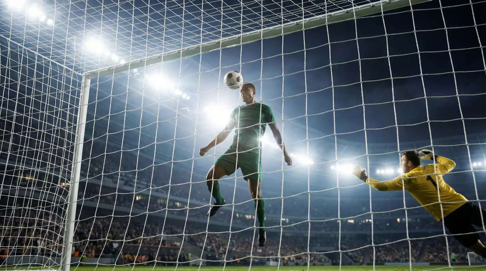 Delantero de fútbol a punto de rematar de cabeza frente a la portería rival bajo focos de estadio