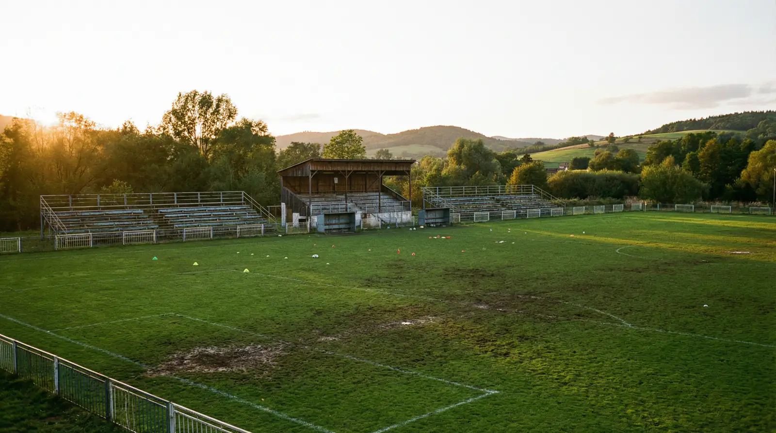 Pequeño estadio de fútbol de una liga menor con gradas modestas y césped natural bajo luz de tarde