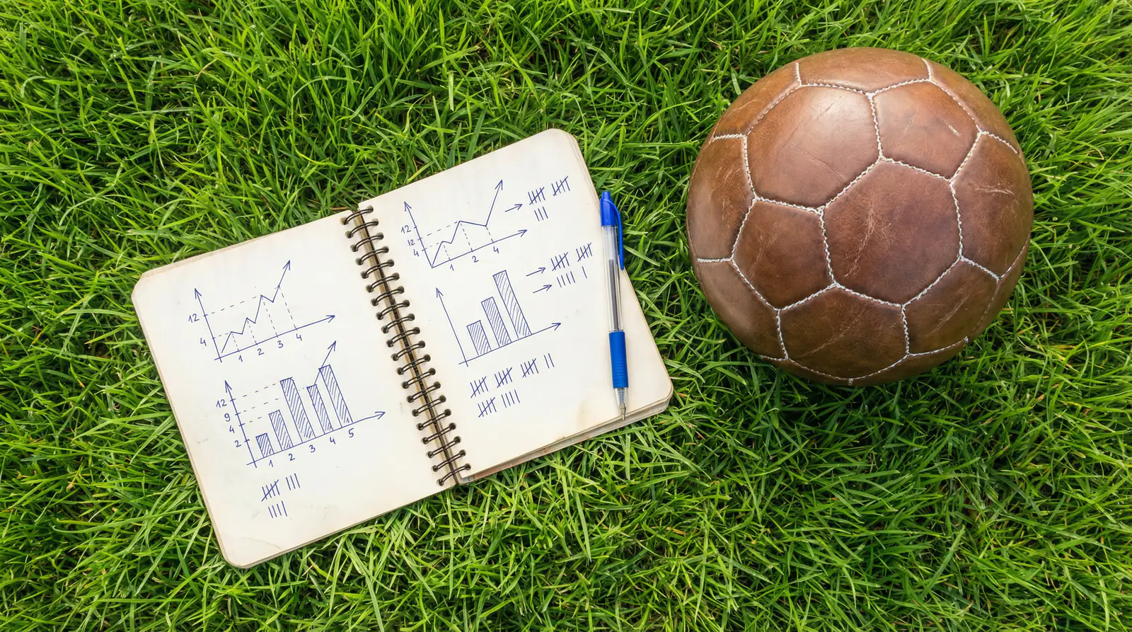 Cuaderno abierto con anotaciones estadísticas de fútbol junto a un balón sobre césped